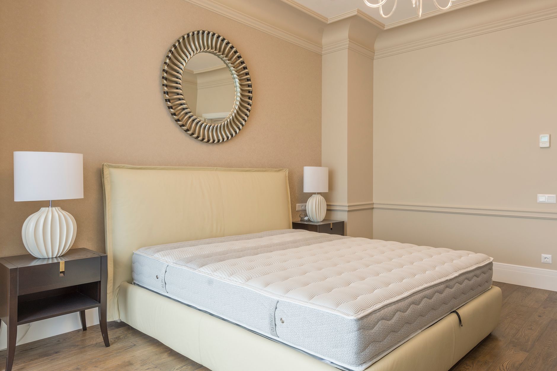 a neatly arranged bedroom featuring a mattress on a bed frame with lamps and a mirror